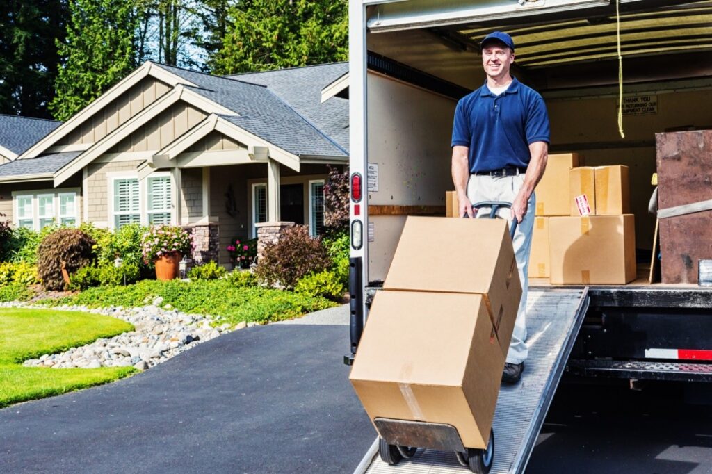 Movers unloading boxes from a truck in front of a house, preparing for a move.