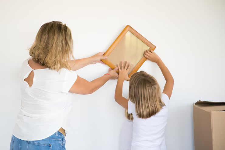 adorable-little-girl-putting-photo-frame-white-wall-with-help-mom