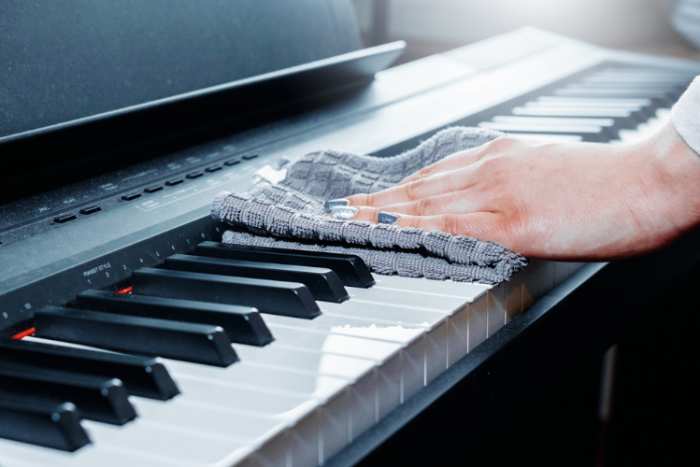 person wiping the keys on the upright piano